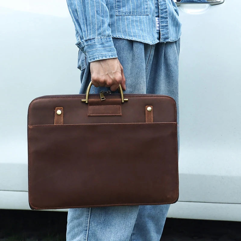 Homme tenant un cartable en cuir marron devant une voiture blanche